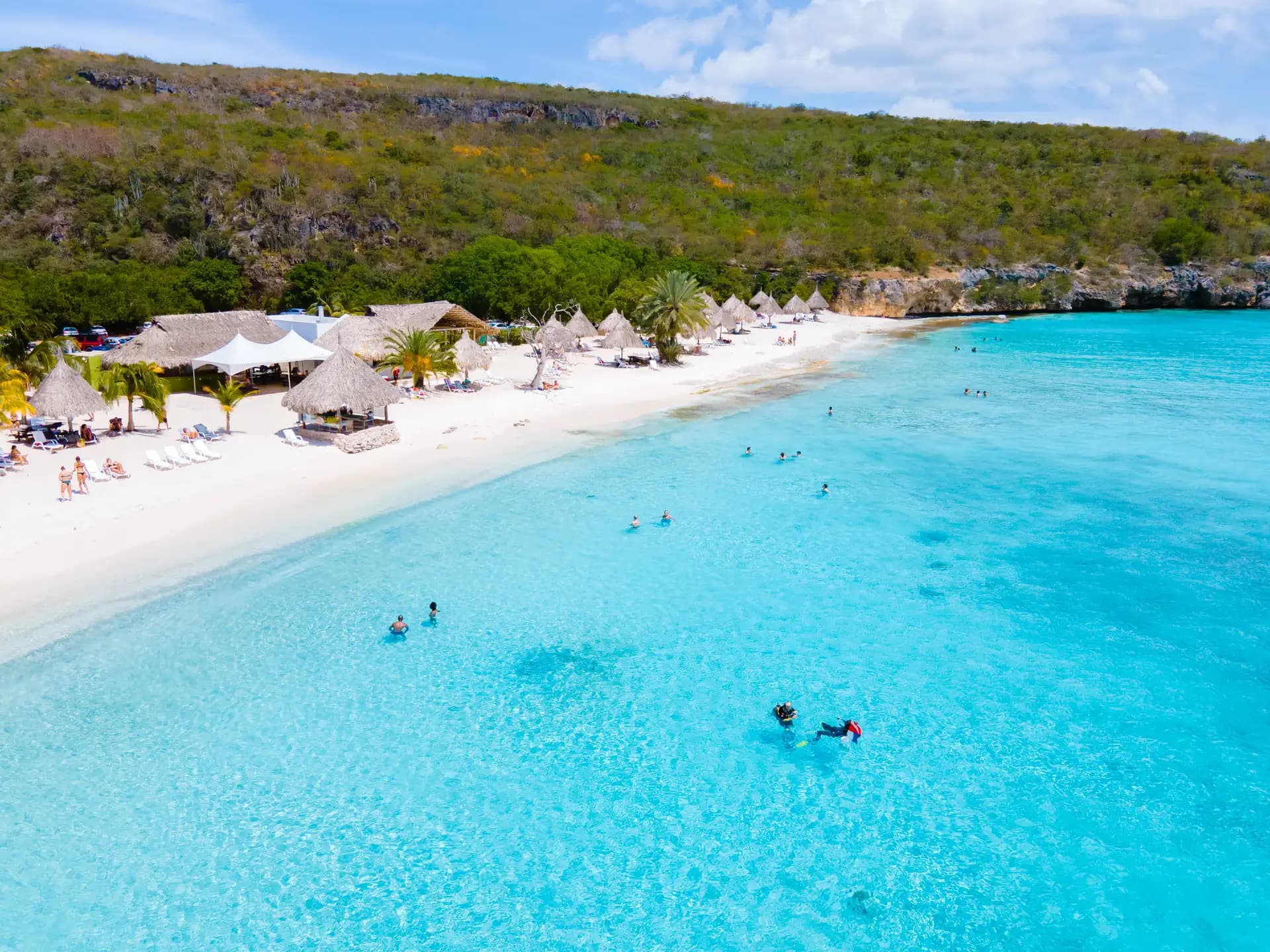 Aerial view of Cas Abou bay, swimmers in clear turquoise shallows below a green headland, Curaçao