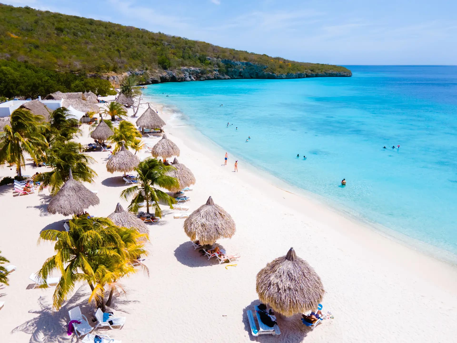 Thatched palapas and palms along the white sand of Cas Abou beach, with turquoise water beyond, Curaçao